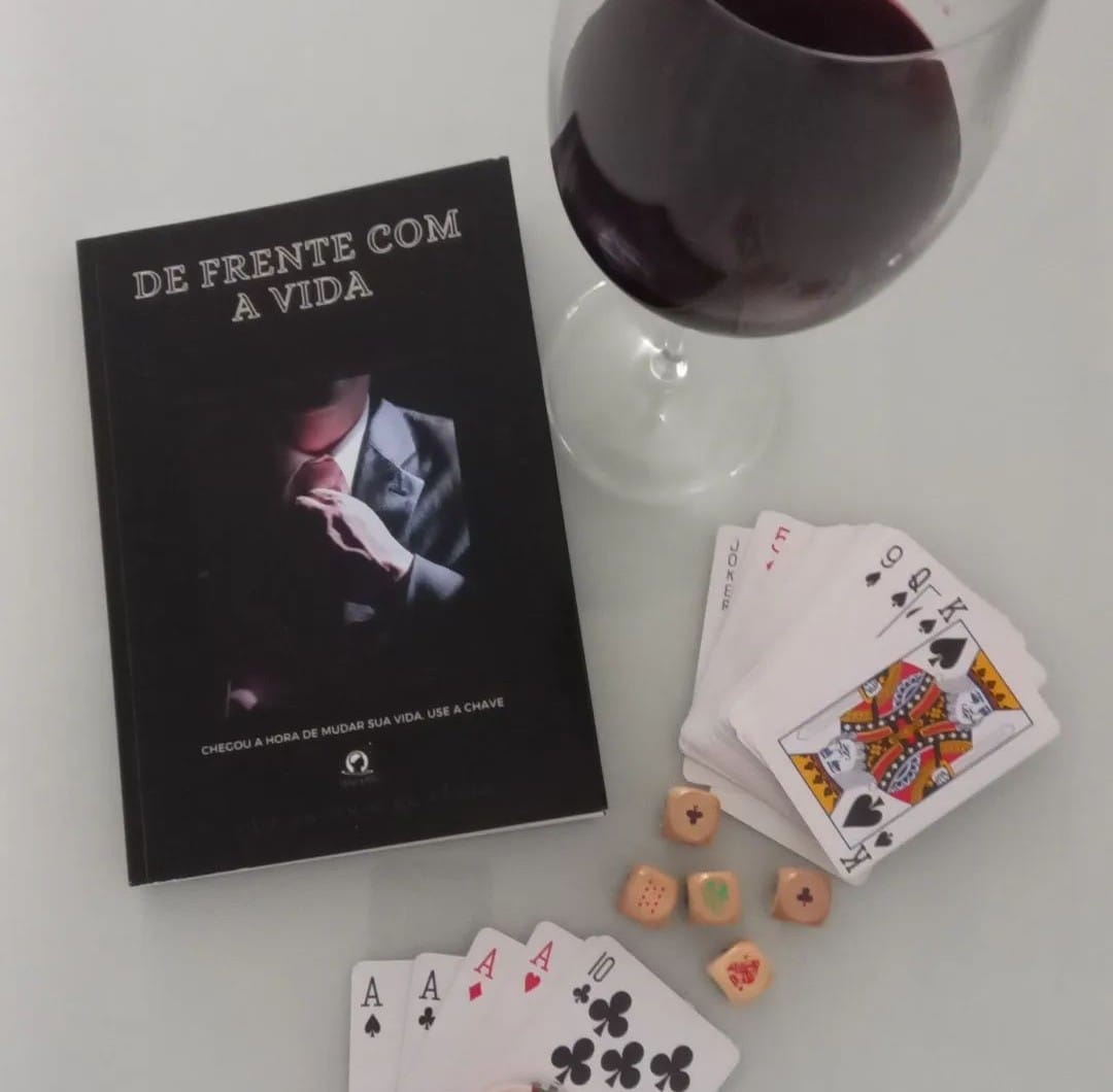 O livro De frente com a vida com um copo de vinho, um baralho semi aberto e alguns dados.