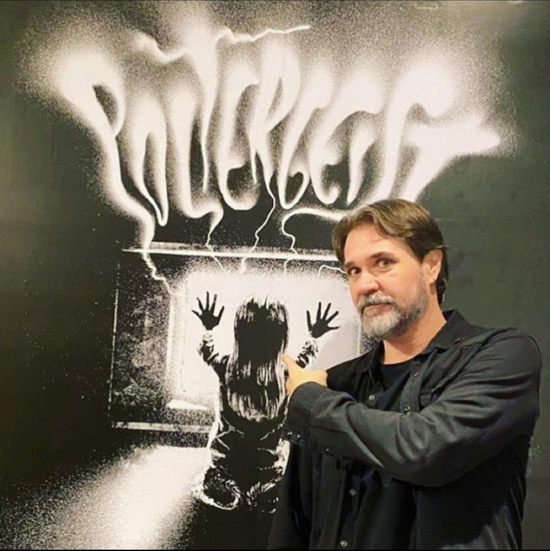 Autor César Bravo em frente a um poster de do filme Poltergeist.